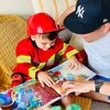 Niño vestido de bombero leyendo su libro DIY sobre él y su papá.